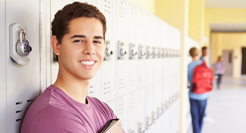 Latino student standing in front of lockers in a hallway.
