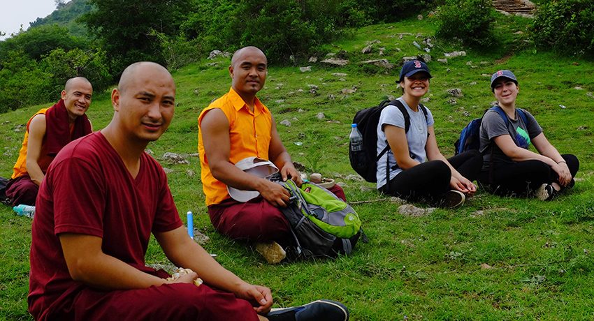 Worcester State University students sit on hillside with monks from Namdroling Monastery in India.