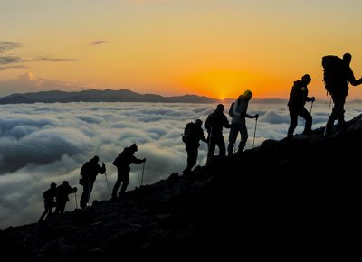 Hikers climbing the mountain above the clouds at sunset.